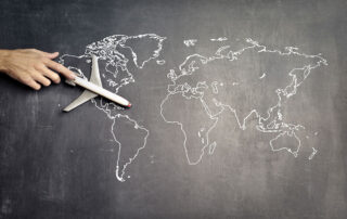 World map on a chalkboard with hand moving a toy airplane