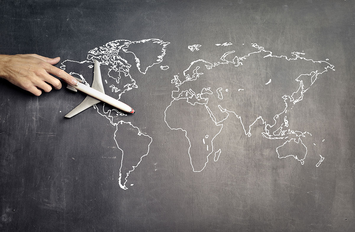 World map on a chalkboard with hand moving a toy airplane